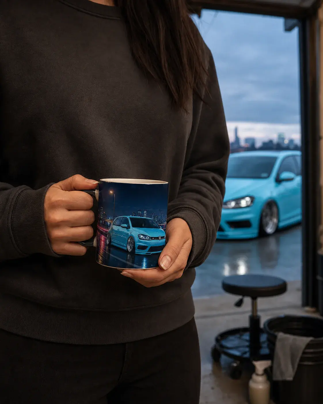 Tasse mit einem hellblauen Golf in der Hand, draußen vor der Garage steht dasselbe Auto